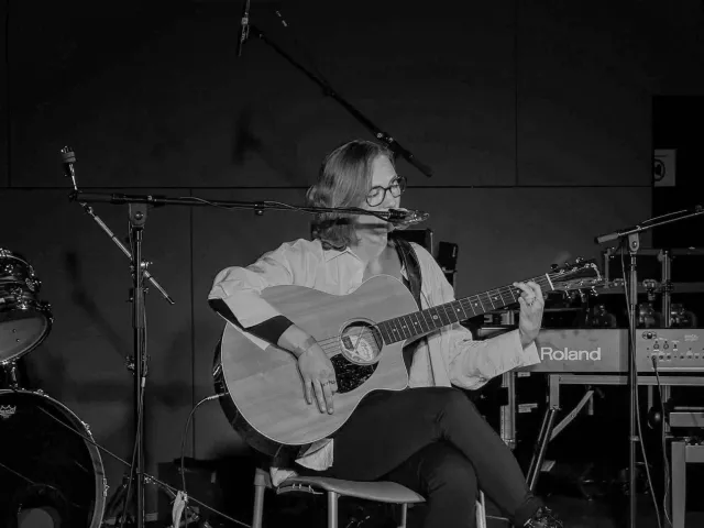 Yasmin playing acoustic guitar and singing at music contest Goeie Vangst, seated, black-and-white
