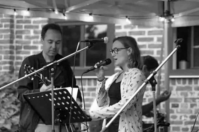 Yasmin singing with a jam band at an outdoor opening event, black-and-white