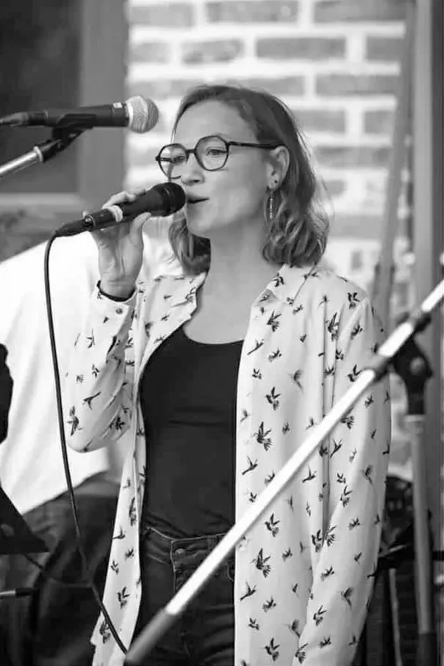 Yasmin performing lead vocals at an outdoor opening event, white floral blouse over a black top, black-and-white